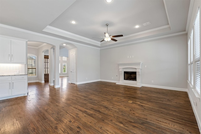 unfurnished living room with visible vents, a fireplace with raised hearth, ceiling fan, dark wood finished floors, and a tray ceiling