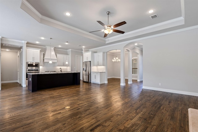 unfurnished living room featuring dark wood-style floors, visible vents, a tray ceiling, arched walkways, and ceiling fan with notable chandelier