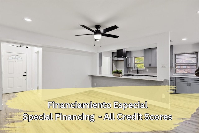 kitchen featuring ceiling fan, light wood-type flooring, gray cabinets, a peninsula, and wall chimney exhaust hood