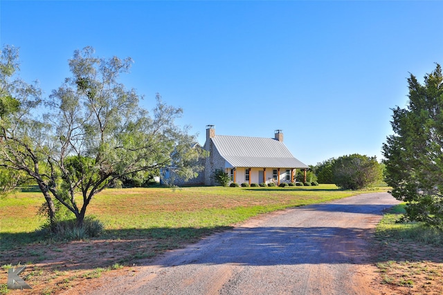 view of front facade featuring driveway, a chimney, a front lawn, and metal roof