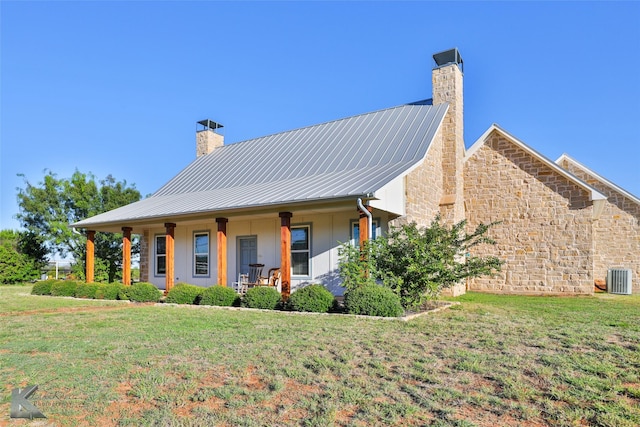 exterior space with a front lawn, central AC, covered porch, metal roof, and a chimney