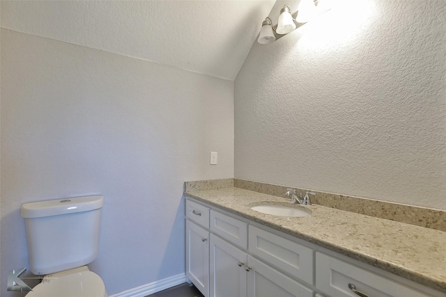 half bath with toilet, vanity, lofted ceiling, and a textured wall