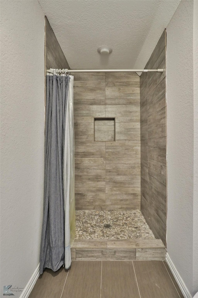 bathroom featuring a textured wall, a tile shower, and a textured ceiling