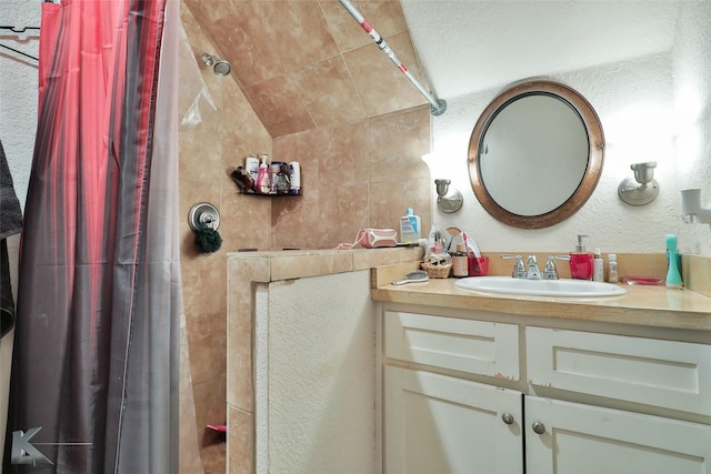 bathroom with tiled shower, vanity, and a textured wall