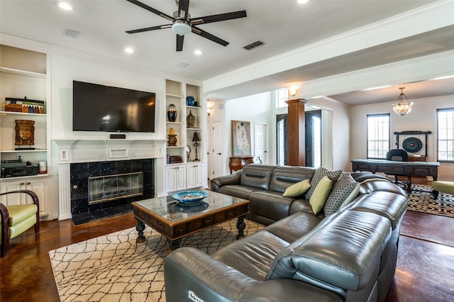 living room featuring visible vents, crown molding, built in features, a fireplace, and a ceiling fan