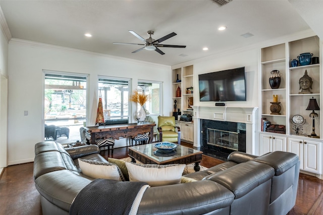 living room featuring ceiling fan, a premium fireplace, ornamental molding, recessed lighting, and dark wood-style flooring