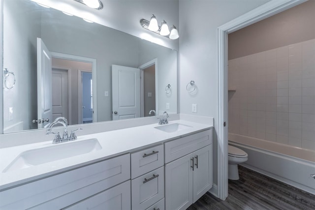 bathroom featuring double vanity, toilet, a sink, and wood finished floors