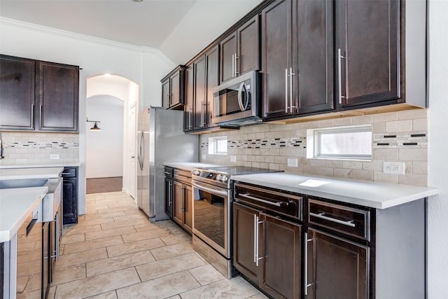 kitchen featuring lofted ceiling, dark brown cabinetry, arched walkways, and appliances with stainless steel finishes