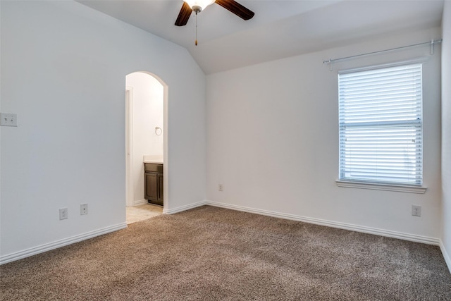 empty room with baseboards, ceiling fan, light colored carpet, lofted ceiling, and arched walkways