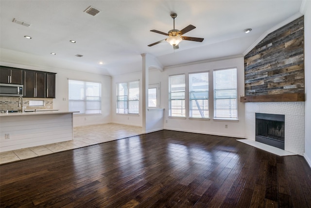 unfurnished living room featuring light wood-style floors, a healthy amount of sunlight, a large fireplace, and a ceiling fan