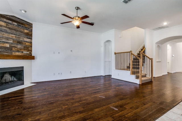 unfurnished living room with stairway, a ceiling fan, visible vents, arched walkways, and ornamental molding