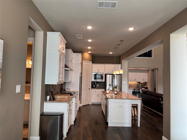 kitchen featuring visible vents, a kitchen bar, white cabinets, stainless steel appliances, and dark wood-style flooring