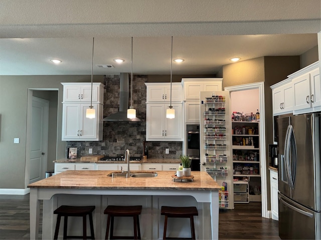 kitchen featuring visible vents, backsplash, wall chimney range hood, appliances with stainless steel finishes, and a sink