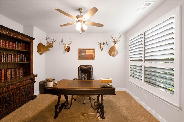 carpeted home office with ceiling fan, baseboards, and visible vents