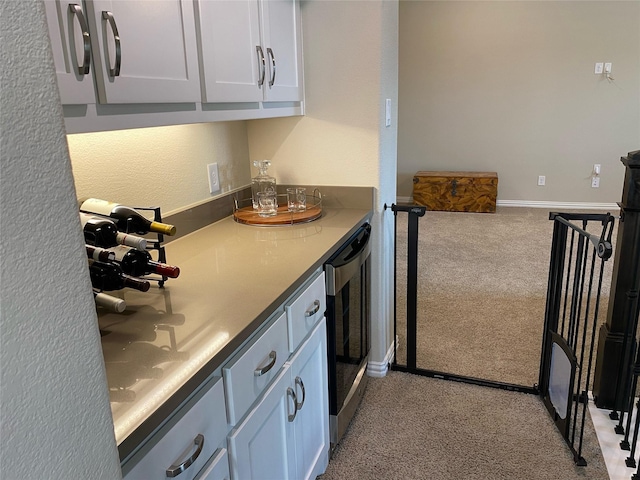 kitchen with beverage cooler, baseboards, light countertops, white cabinetry, and light colored carpet