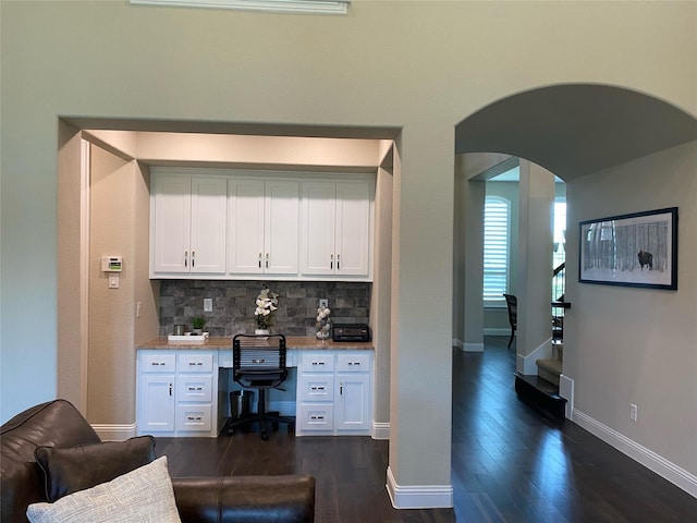 bar with dark wood finished floors, arched walkways, decorative backsplash, baseboards, and built in study area