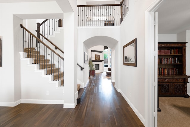 entryway featuring dark wood-style floors, arched walkways, baseboards, a fireplace with raised hearth, and stairway