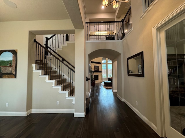 foyer featuring dark wood-style floors, stairway, arched walkways, a high ceiling, and baseboards