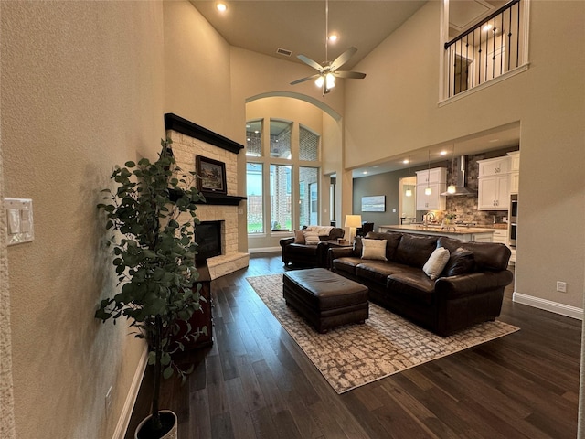 living area featuring dark wood-style floors, a stone fireplace, arched walkways, and a ceiling fan