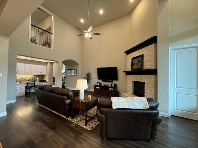 living room with ceiling fan, arched walkways, a fireplace, and dark wood-style flooring