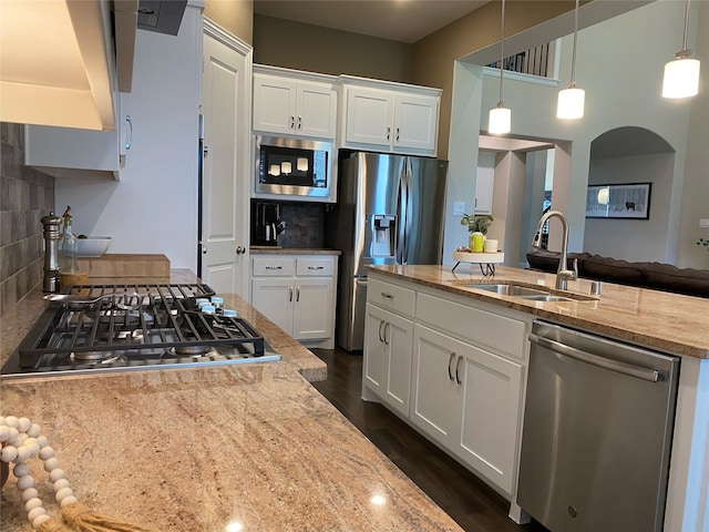 kitchen with light stone countertops, dark wood-style floors, a sink, appliances with stainless steel finishes, and backsplash