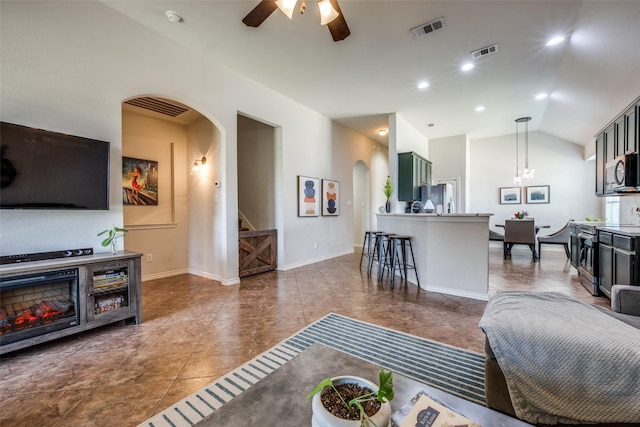 tiled living room with arched walkways, visible vents, ceiling fan with notable chandelier, and stairway