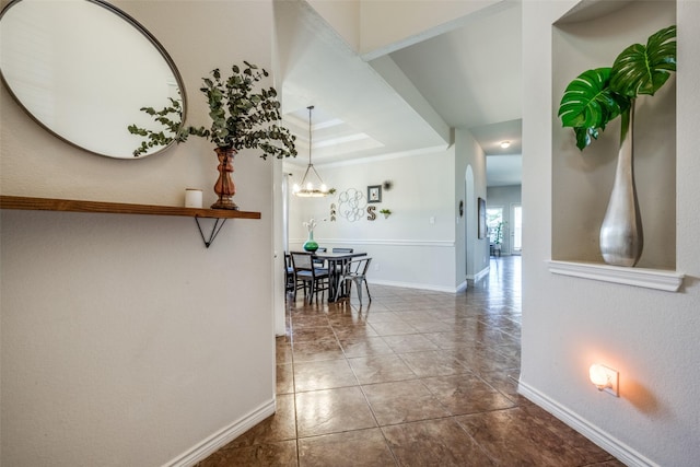 corridor featuring baseboards, a tray ceiling, arched walkways, crown molding, and a notable chandelier