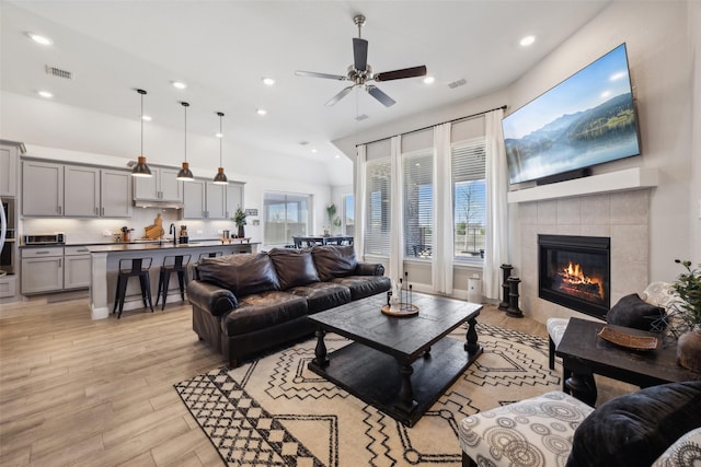 living area with a tile fireplace, a ceiling fan, visible vents, and light wood-type flooring