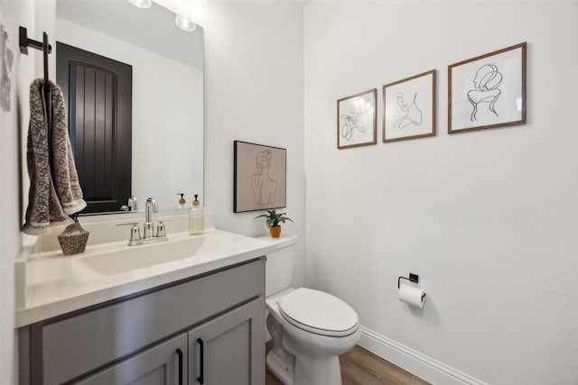 bathroom with toilet, vanity, baseboards, and wood finished floors