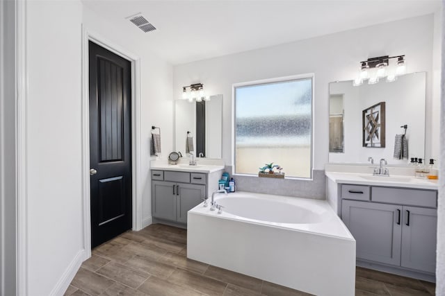 full bath with visible vents, wood finish floors, two vanities, a sink, and a garden tub