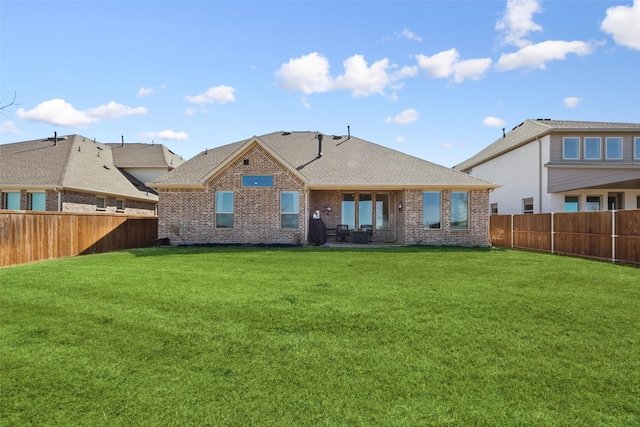 back of house featuring a lawn, brick siding, a fenced backyard, and a shingled roof