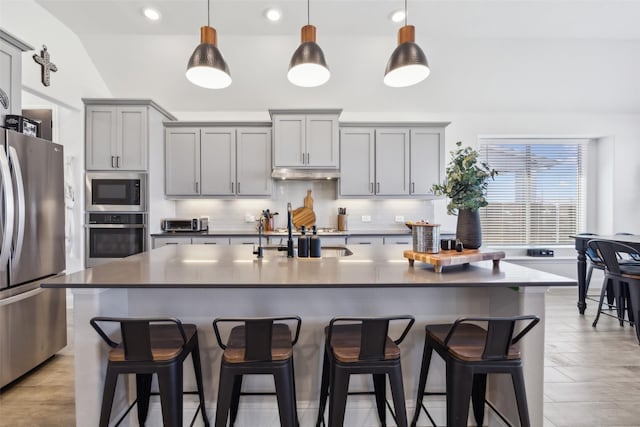 kitchen with under cabinet range hood, gray cabinets, appliances with stainless steel finishes, and tasteful backsplash