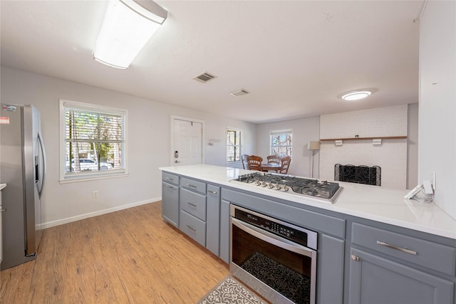 kitchen with visible vents, light wood-type flooring, light countertops, gray cabinets, and stainless steel appliances