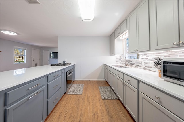 kitchen with light wood finished floors, backsplash, gray cabinets, appliances with stainless steel finishes, and a sink