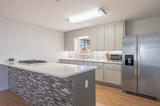 kitchen featuring decorative backsplash, light wood-style flooring, a peninsula, stainless steel appliances, and a sink