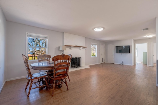 dining space featuring visible vents, baseboards, a brick fireplace, and wood finished floors