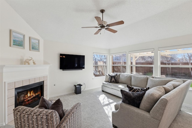 living room with baseboards, carpet floors, lofted ceiling, ceiling fan, and a tiled fireplace