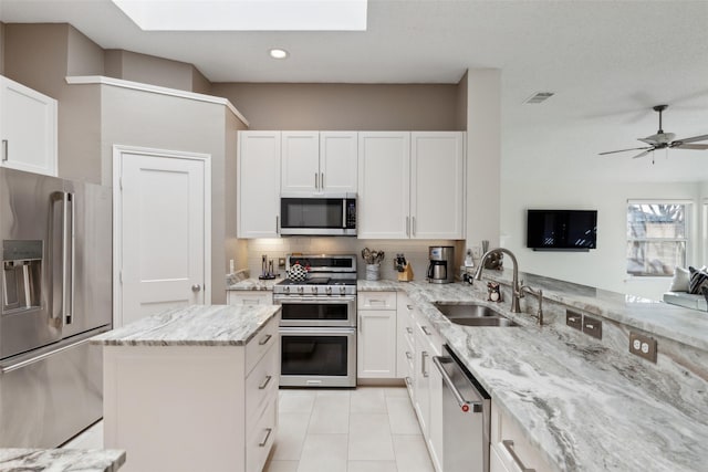 kitchen featuring light stone counters, light tile patterned floors, stainless steel appliances, white cabinetry, and a sink