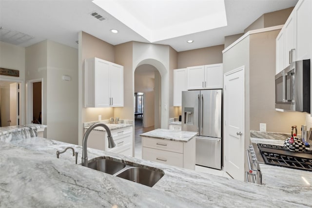 kitchen featuring light stone countertops, arched walkways, white cabinets, stainless steel appliances, and a sink