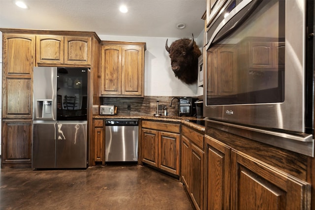 kitchen with a sink, tasteful backsplash, stainless steel appliances, dark stone counters, and concrete flooring