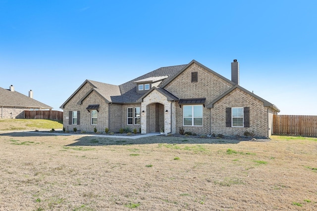 french country style house featuring brick siding, a front lawn, and fence