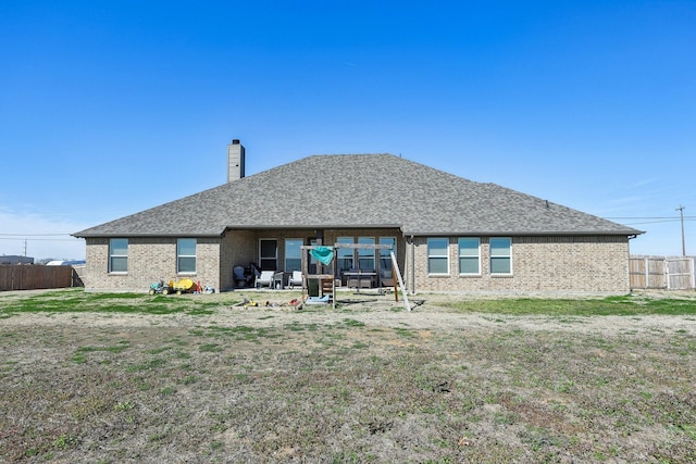 back of house featuring fence, roof with shingles, a chimney, a lawn, and brick siding