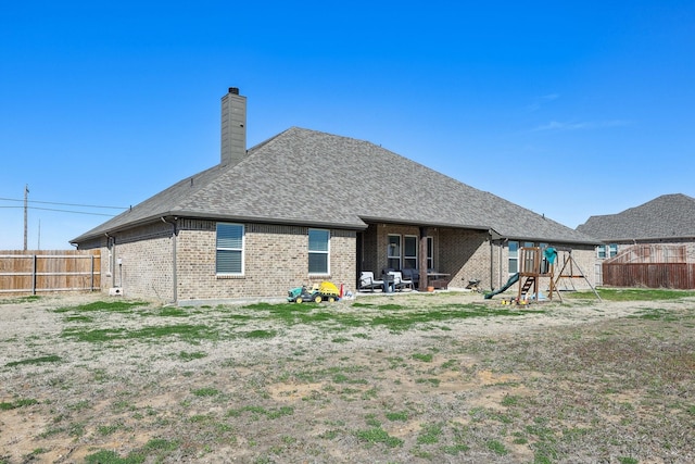 rear view of property with a playground, a fenced backyard, brick siding, and a chimney