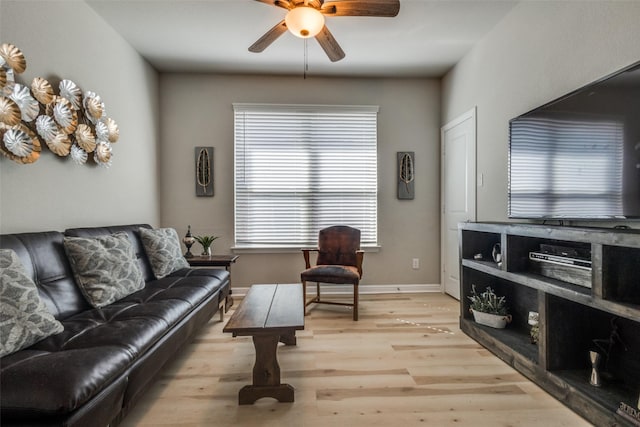 living area featuring baseboards, light wood-type flooring, and ceiling fan