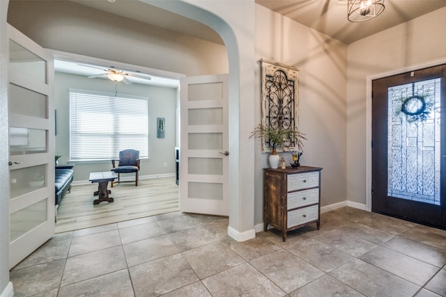 entrance foyer featuring a ceiling fan, light tile patterned floors, baseboards, and arched walkways