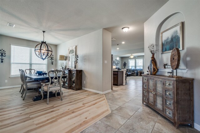 dining space featuring visible vents, baseboards, light tile patterned flooring, and ceiling fan with notable chandelier