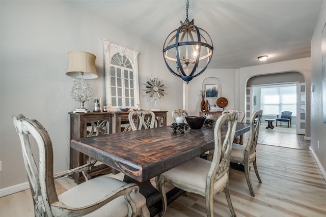 dining room with arched walkways, a notable chandelier, baseboards, and light wood-style floors