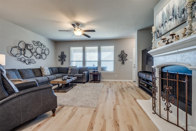 living area with a fireplace, baseboards, light wood-type flooring, and ceiling fan