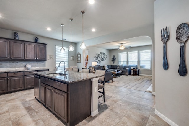 kitchen featuring a breakfast bar, dark brown cabinetry, stainless steel dishwasher, and a sink