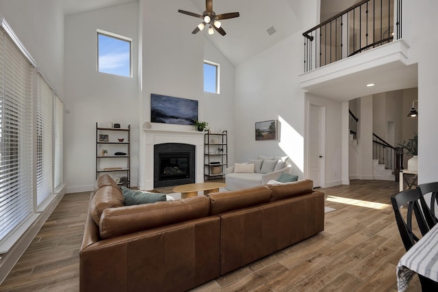 living room with wood finished floors, baseboards, a ceiling fan, stairs, and a glass covered fireplace